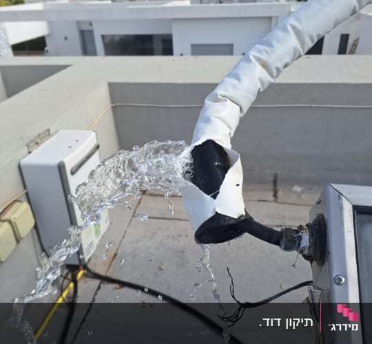 מים זורמים מצינור על גג עם רקע של בניינים.